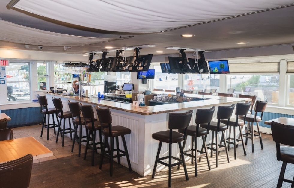 Bar with stools, TVs, and a white counter; windows and light-colored wood walls.