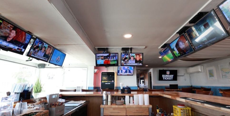 Bar interior with multiple televisions showing sports; bar counter and patrons in the background.