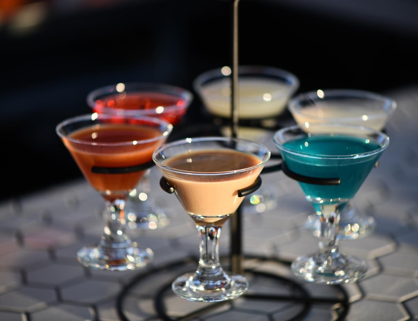 Five colorful cocktails in stemmed glasses on a tiered stand.