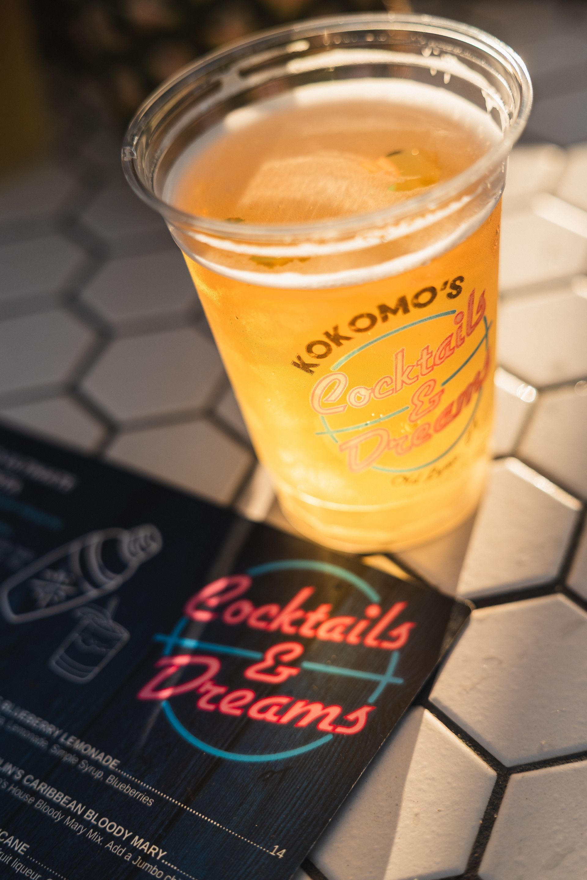 A cup of cocktail and a menu on a white tiled surface.
