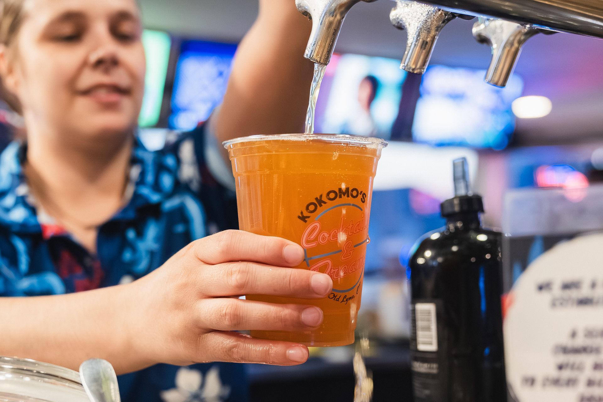 Bartender pouring a drink from a tap into a plastic cup.