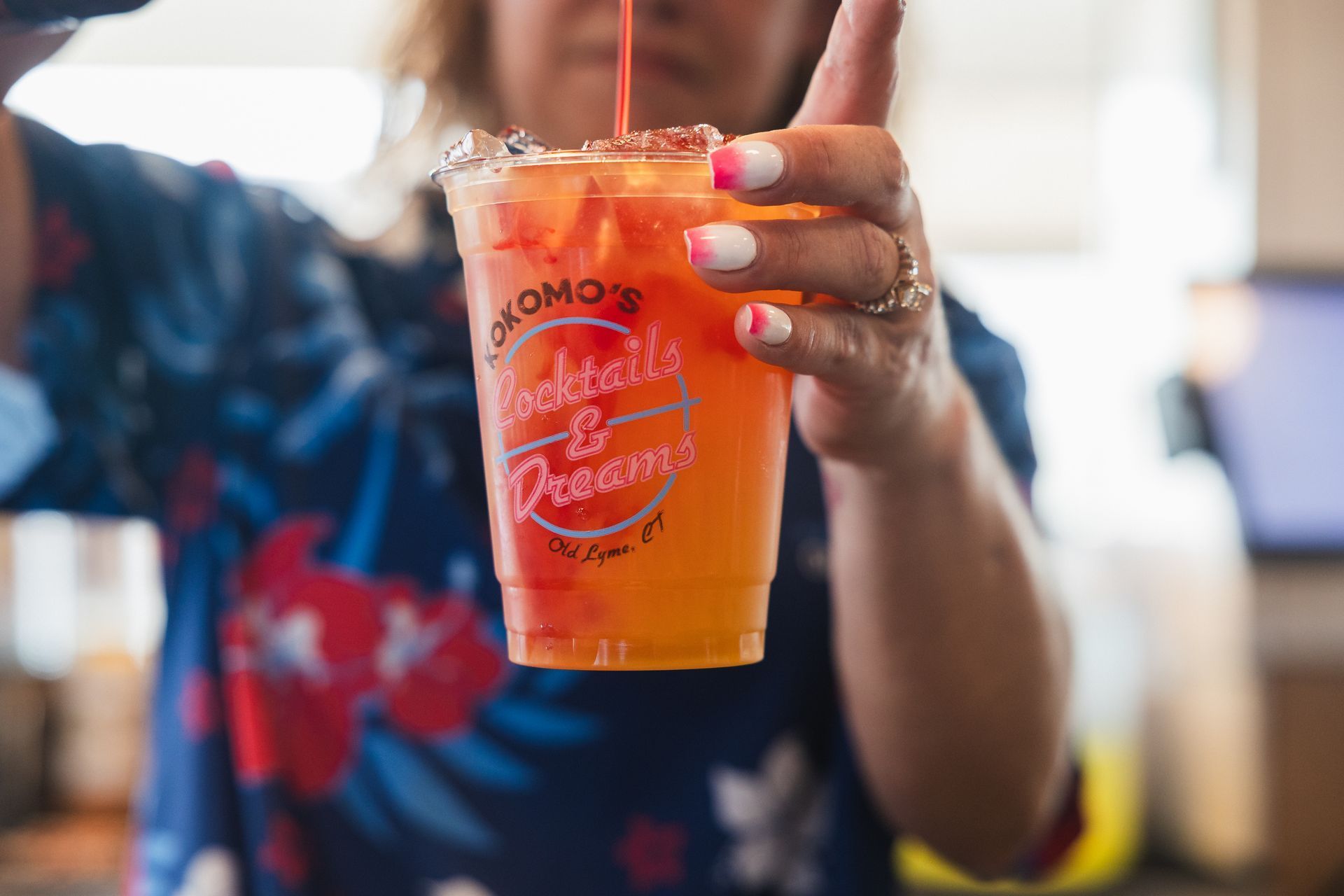 Bartender pouring a layered, orange and red cocktail in a clear cup.