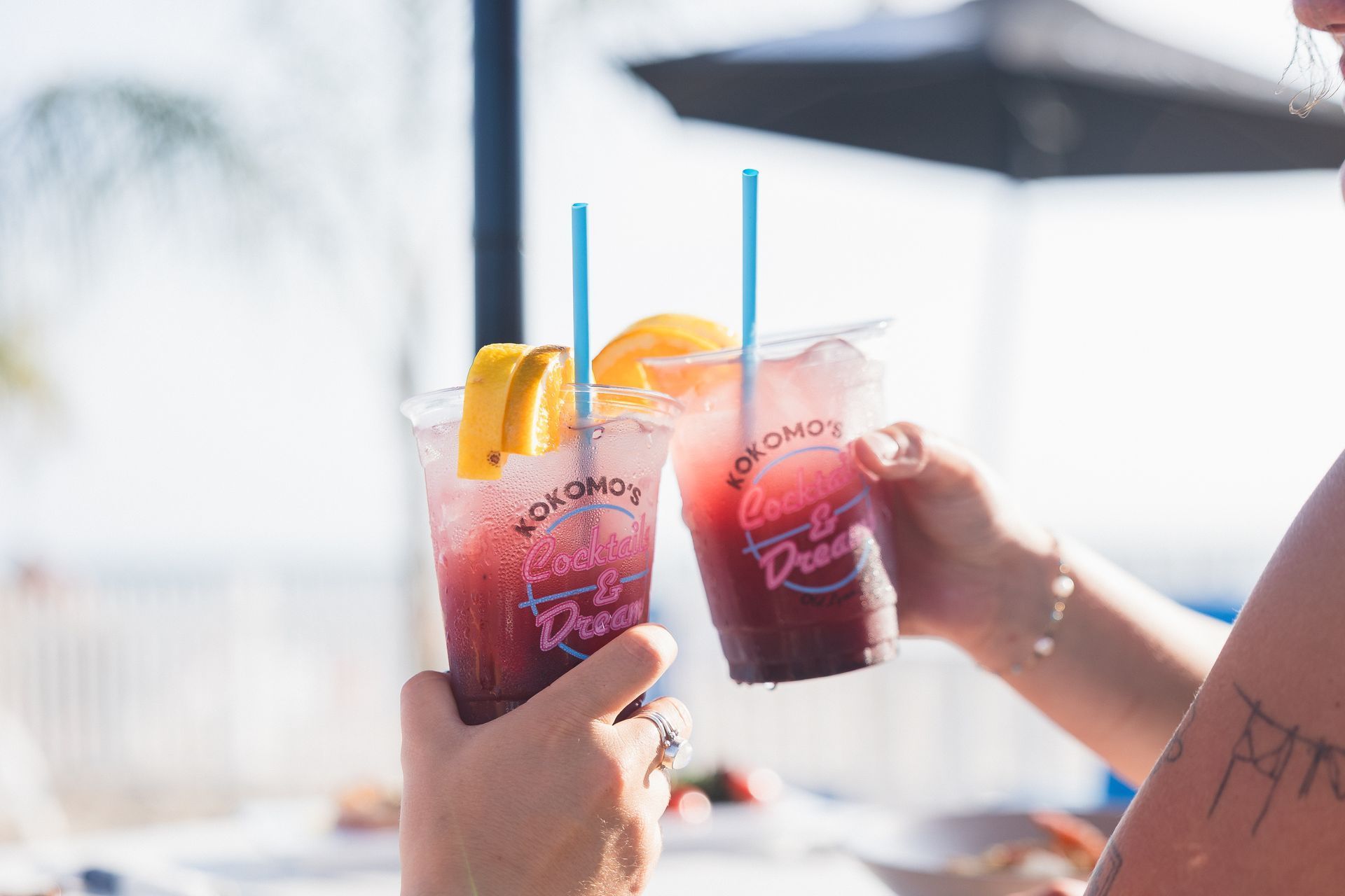 Two people toasting colorful drinks with fruit garnishes.