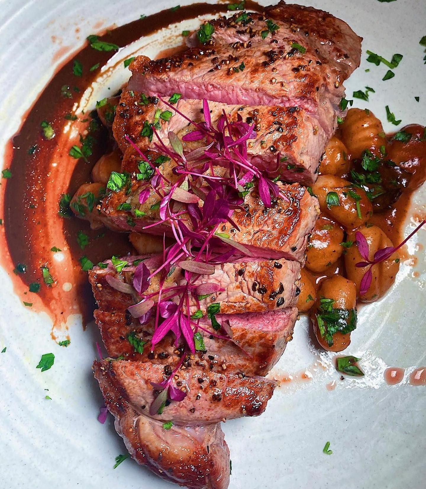 A close up of a plate of food with meat and beans on a table.