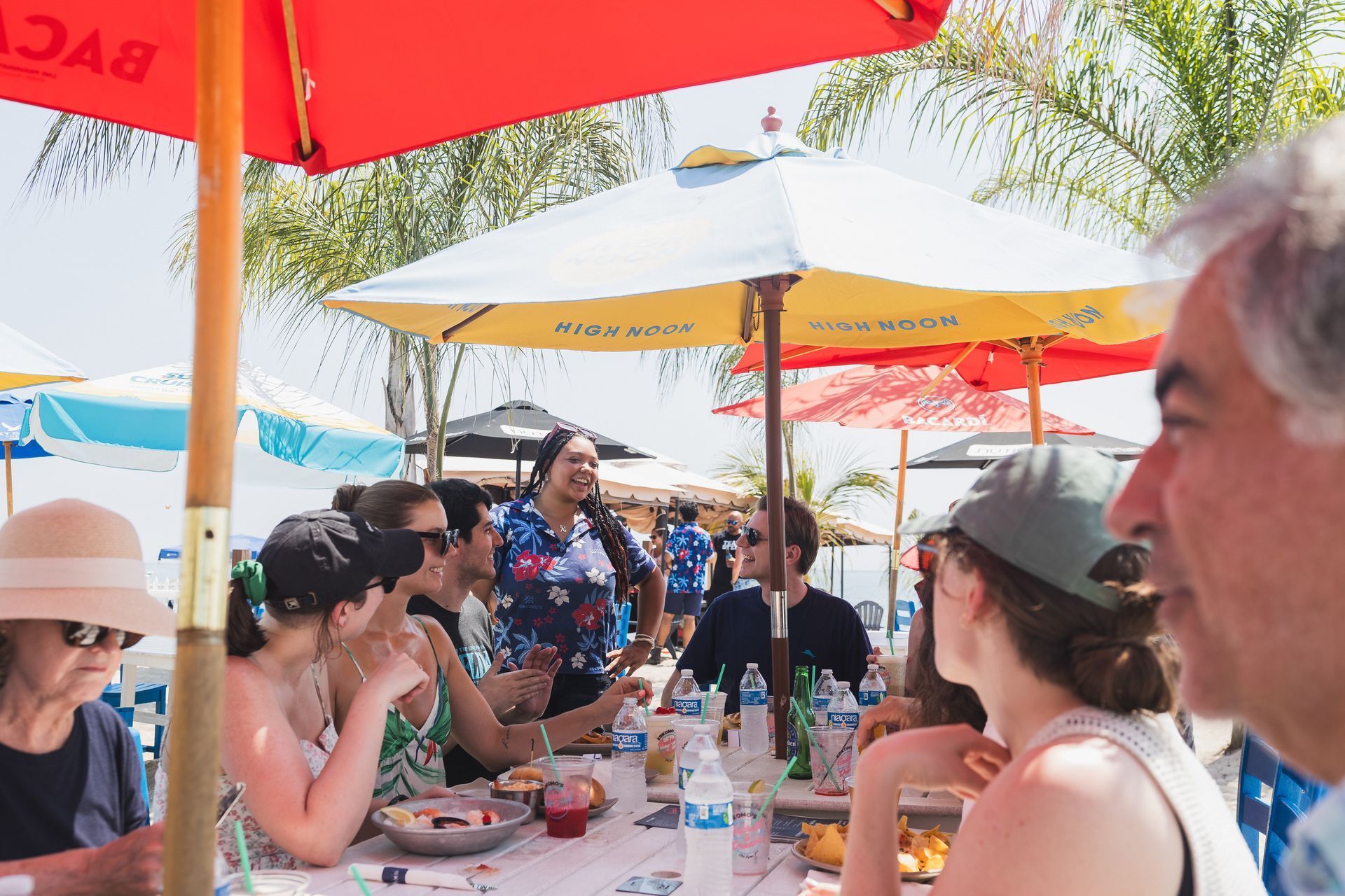 Group of people at outdoor restaurant under umbrellas, eating and talking.