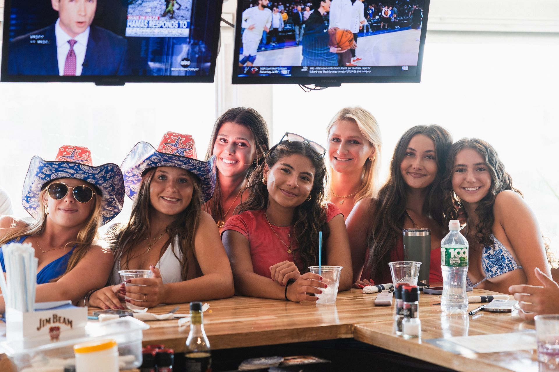 Group of young women at a bar, some wearing patriotic hats, smiling at the camera.