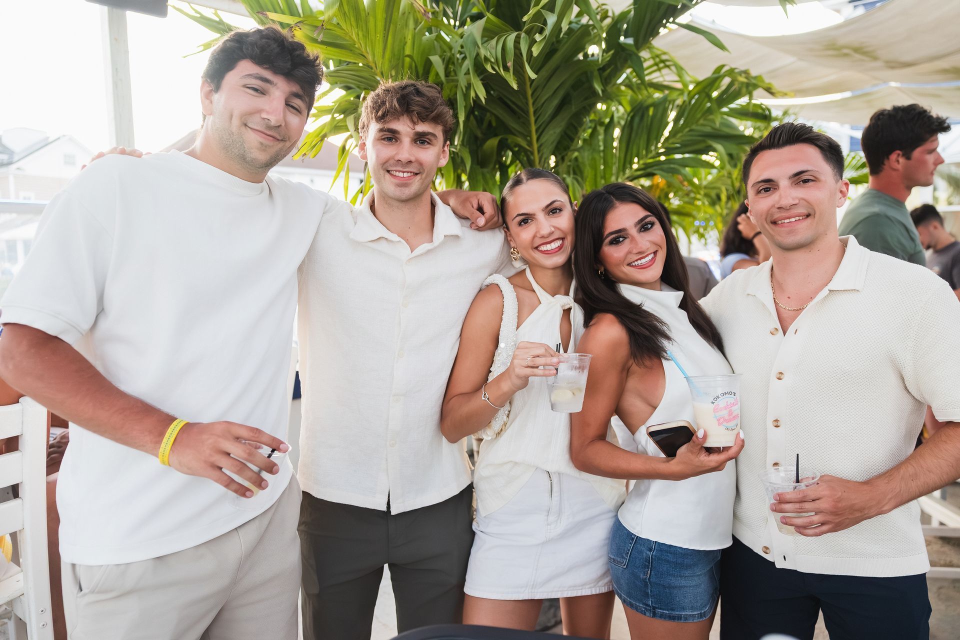 Group of five smiling people dressed in white at outdoor event.