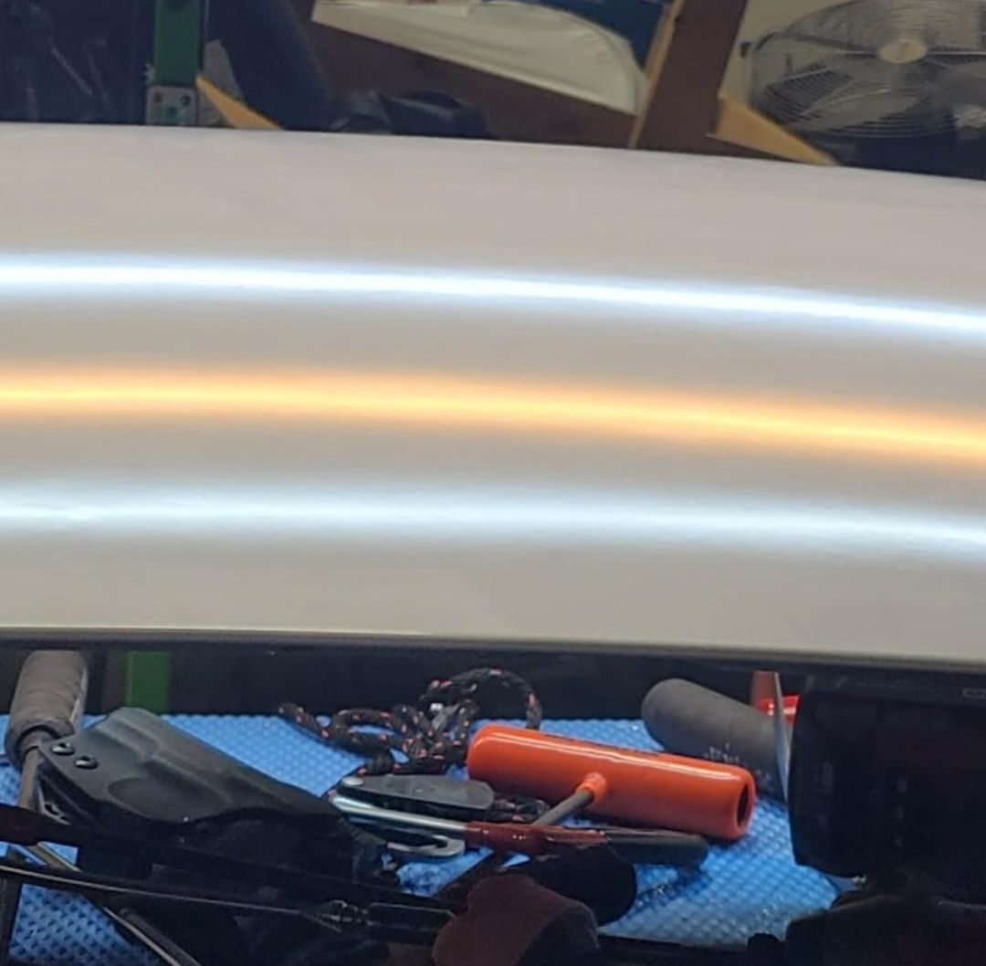 Car panel reflecting light, showing a dent with tools in the foreground on a blue mat.