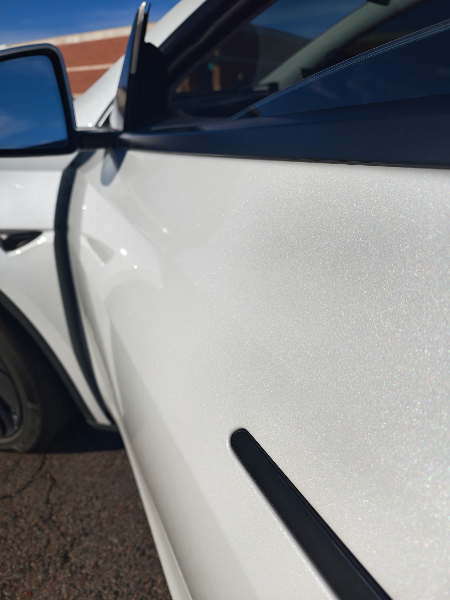 White car door with black trim and a sparkly finish; blue sky in background.