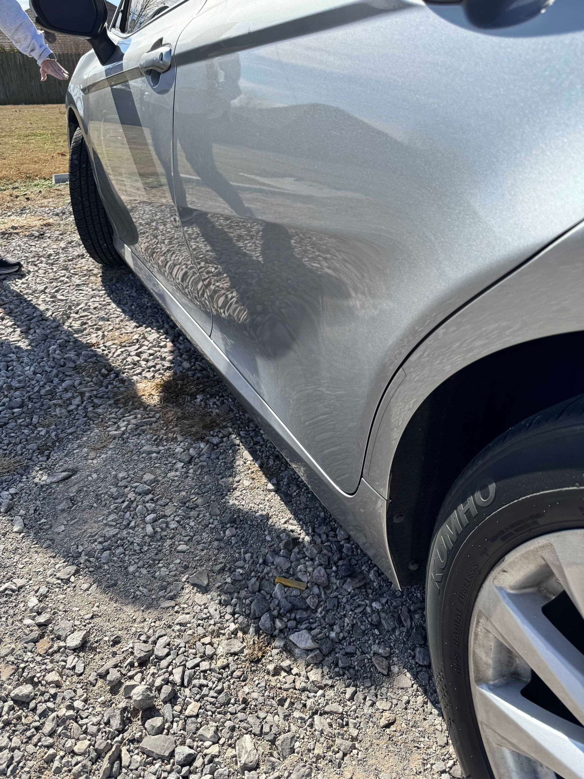 Silver car parked on gravel.