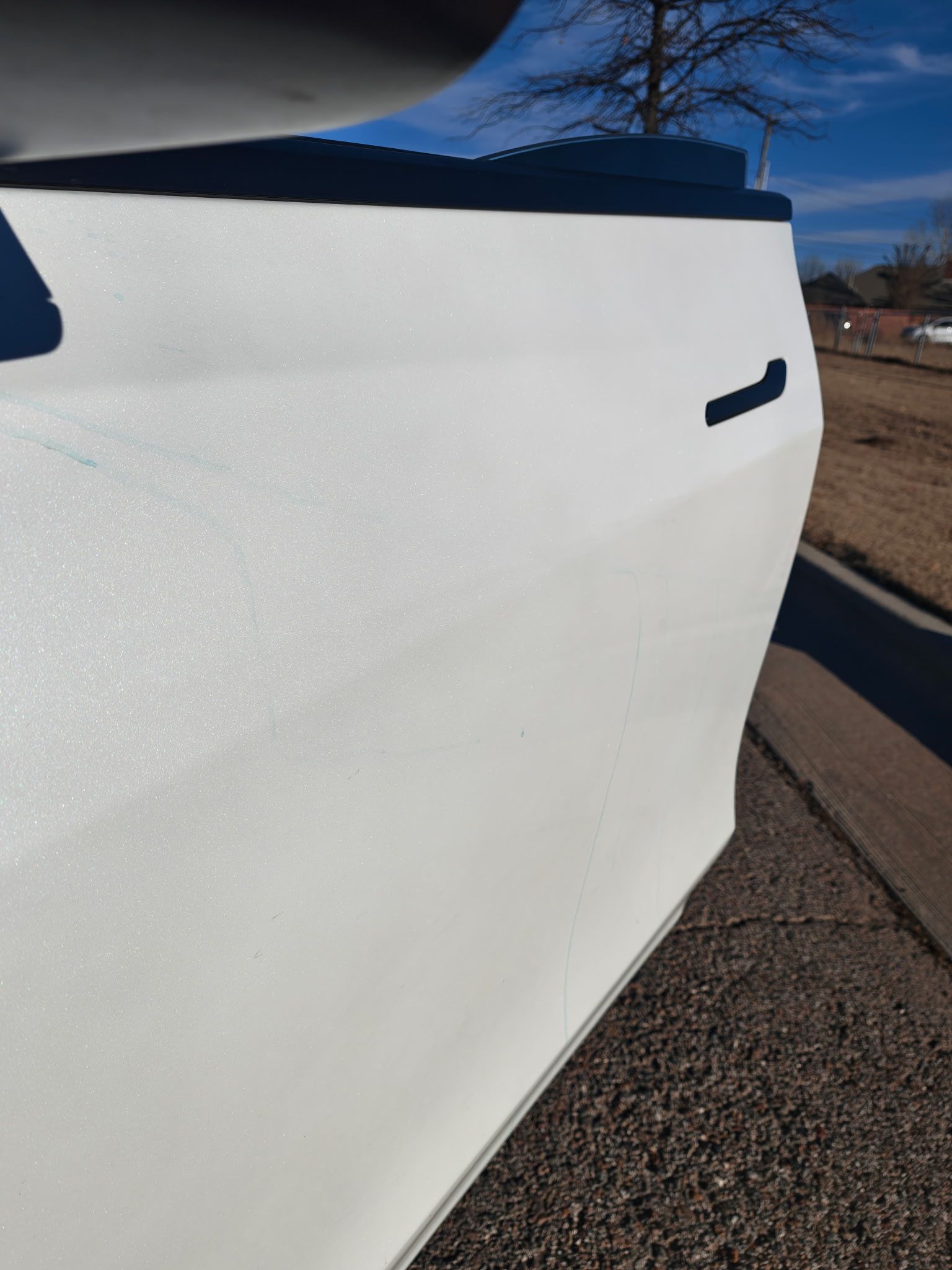 White car side panel on gravel driveway with blue sky visible.