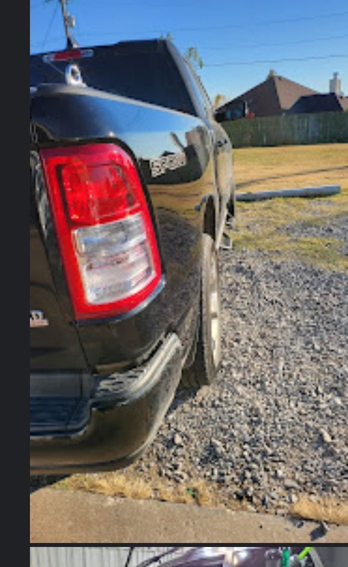 Black pickup truck's rear side with taillight, parked on gravel. Daytime, exterior shot.