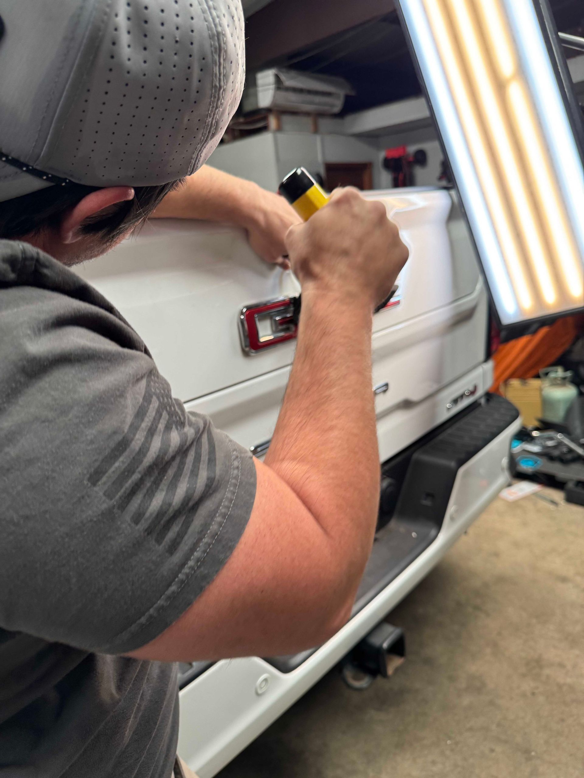 Person using a tool to repair a white car's rear, under a light.