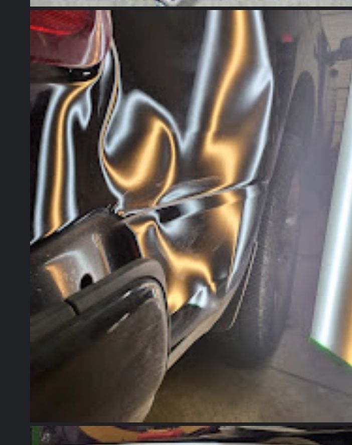 Damaged black car rear quarter panel, dented and distorted with reflection.