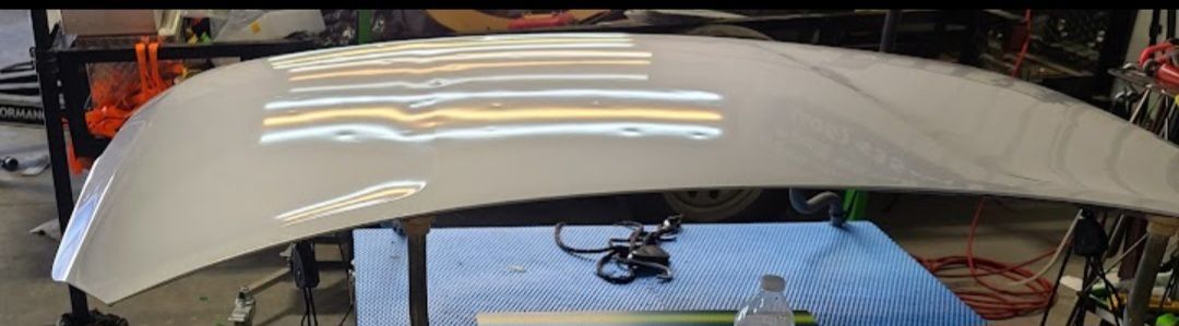 Car hood with dents, being inspected under shop lights.