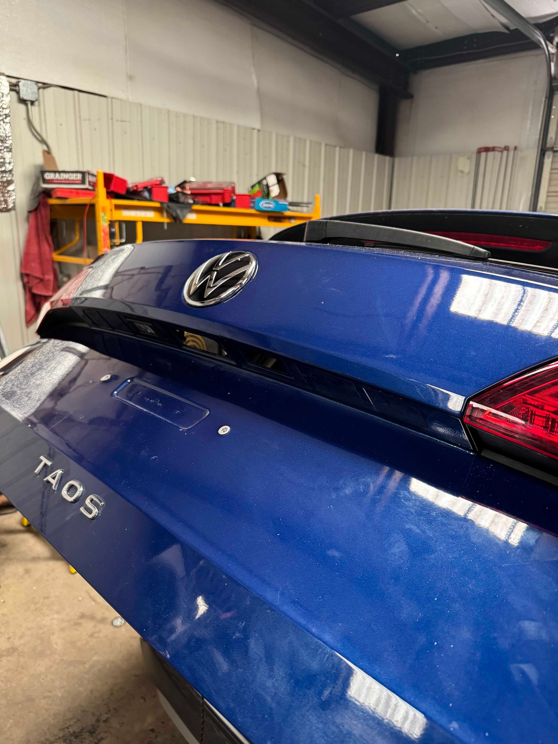 Blue Volkswagen Taos rear with dented liftgate in a repair shop. The Taos emblem is visible.