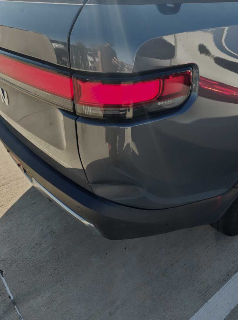 Rear corner of a dark gray SUV, showing taillight and slight dent in bumper.