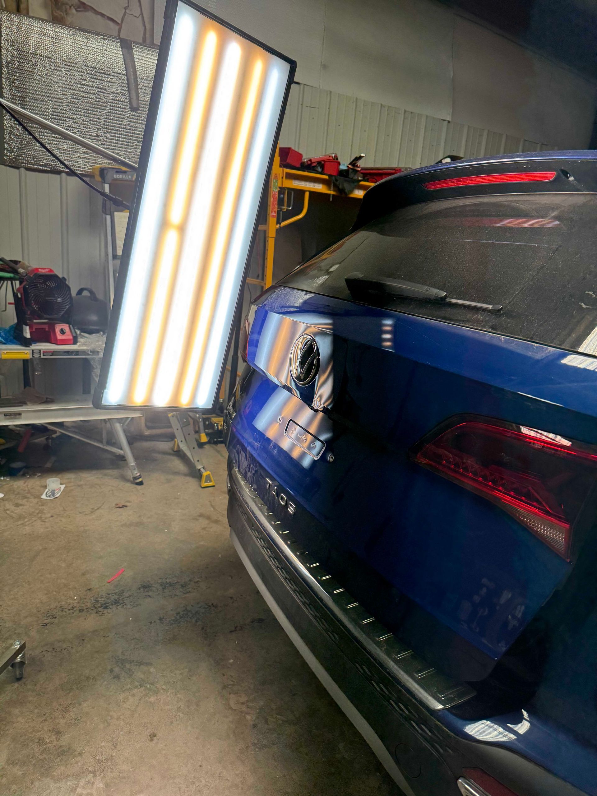 Blue car with dent being repaired with a PDR light in a shop.