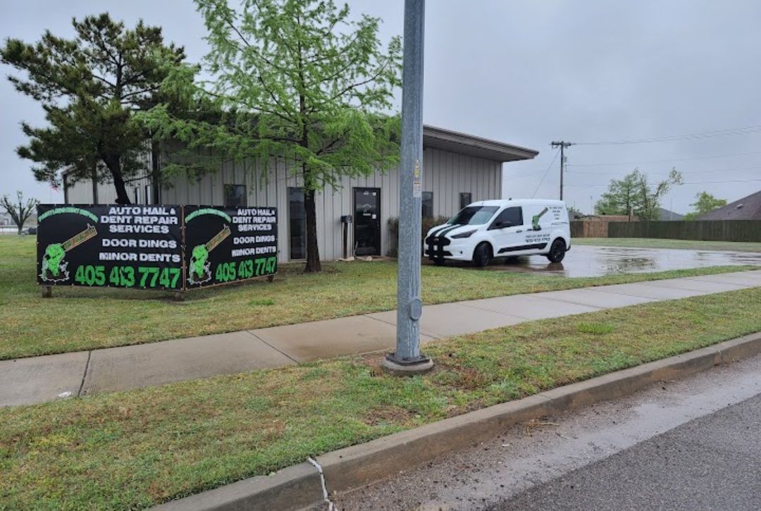 A white van parked outside a building with two signs, a wet street.