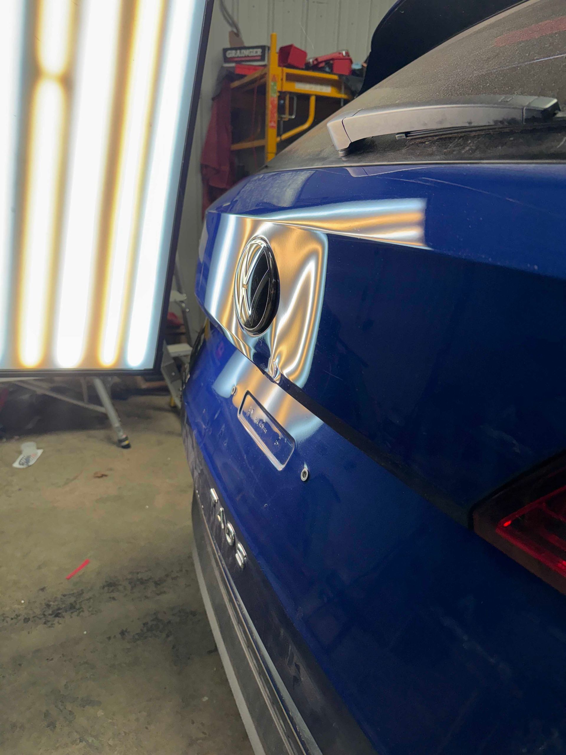 Blue car with dented rear; a light board is positioned near it.