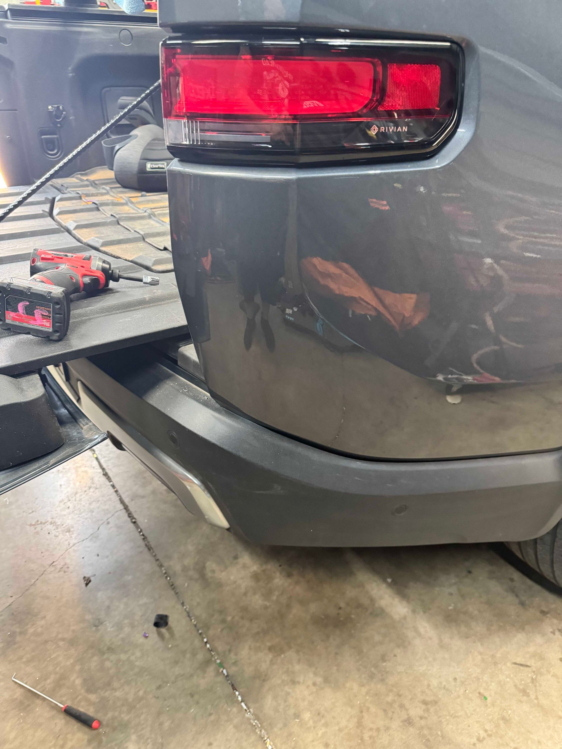 Rear bumper of a gray vehicle with a red taillight and a toolbox in the bed.