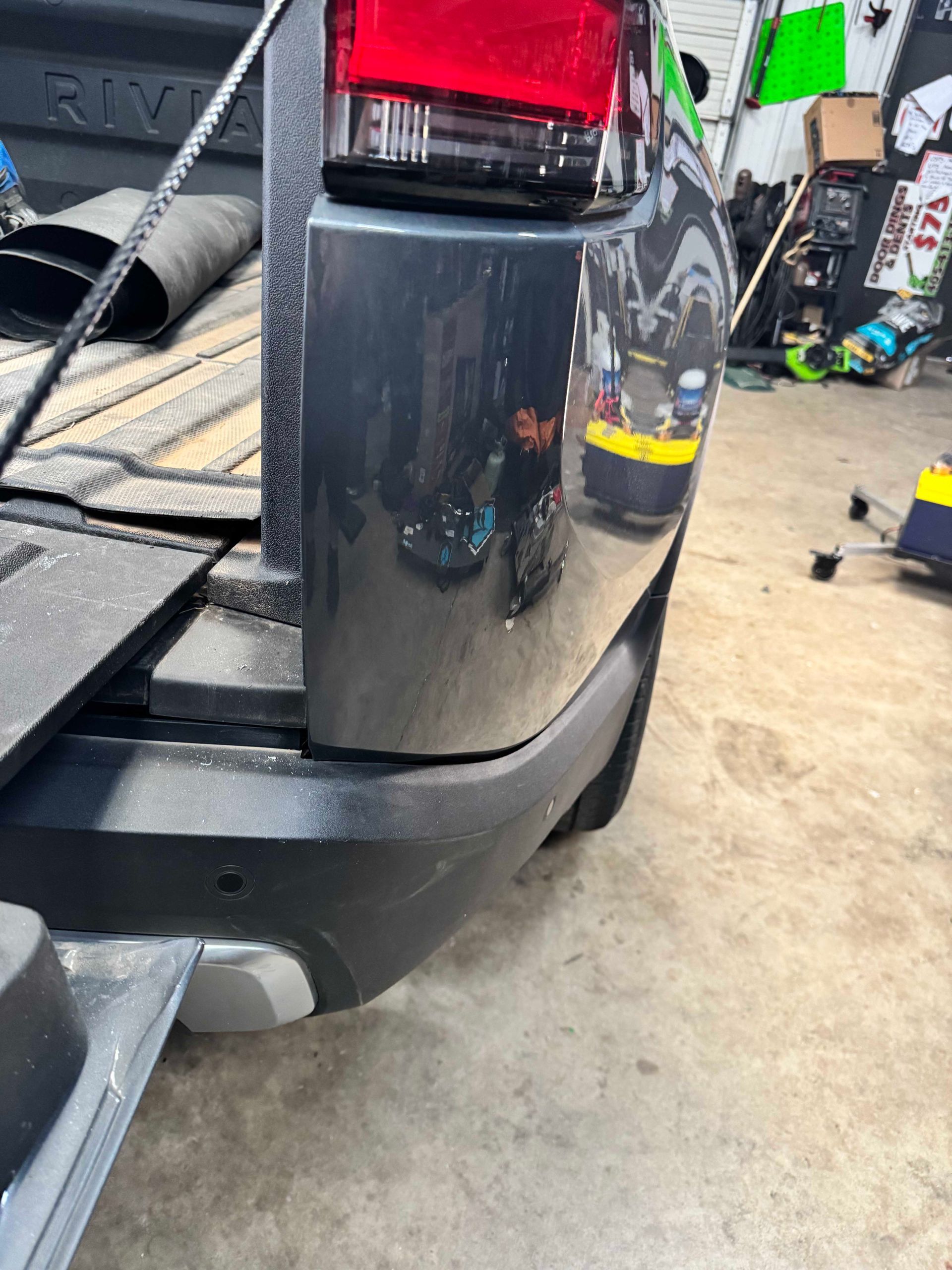 Close-up of a dark grey pickup truck rear corner with a scuffed black bumper and a red taillight.