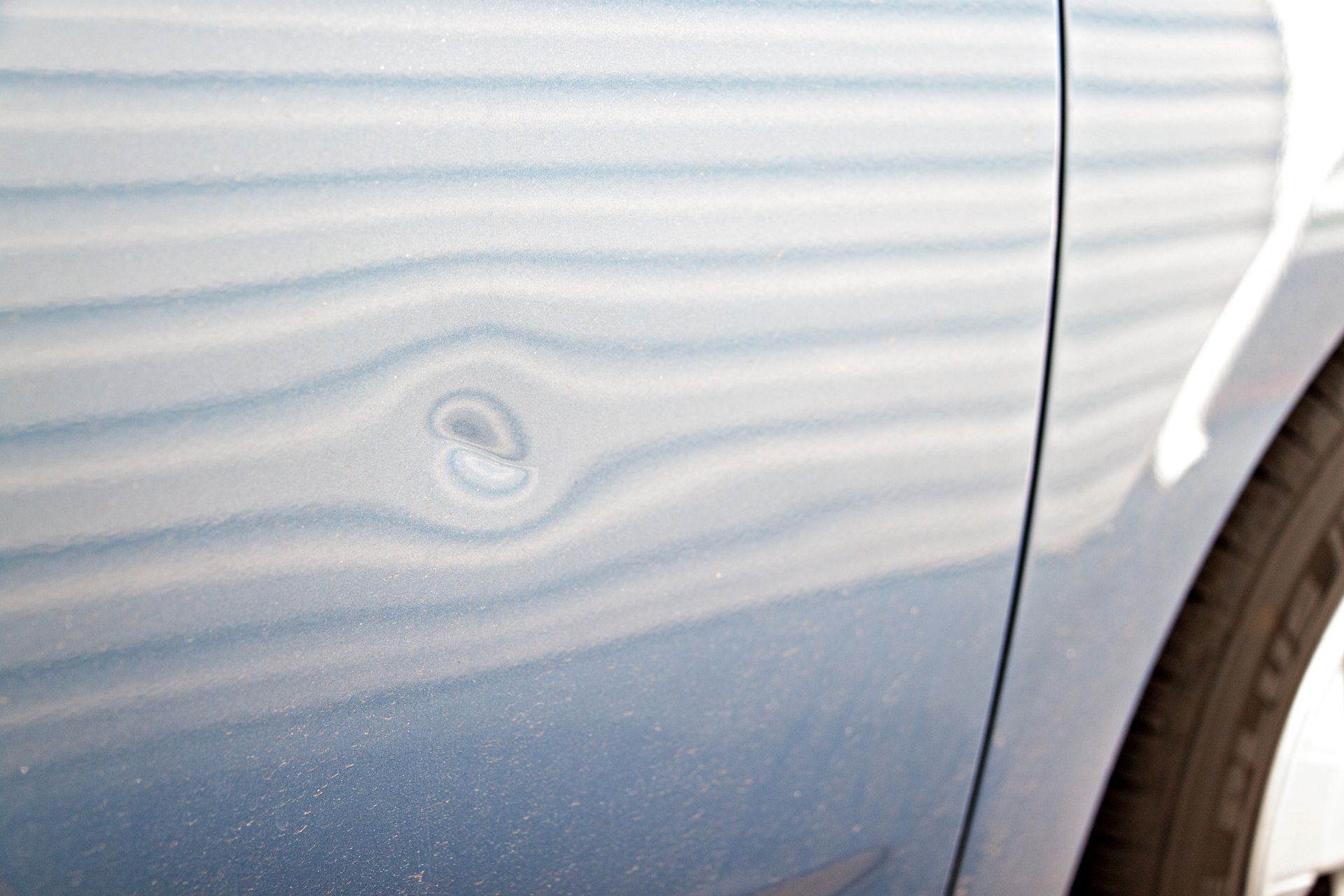 Blue car door with a dent.