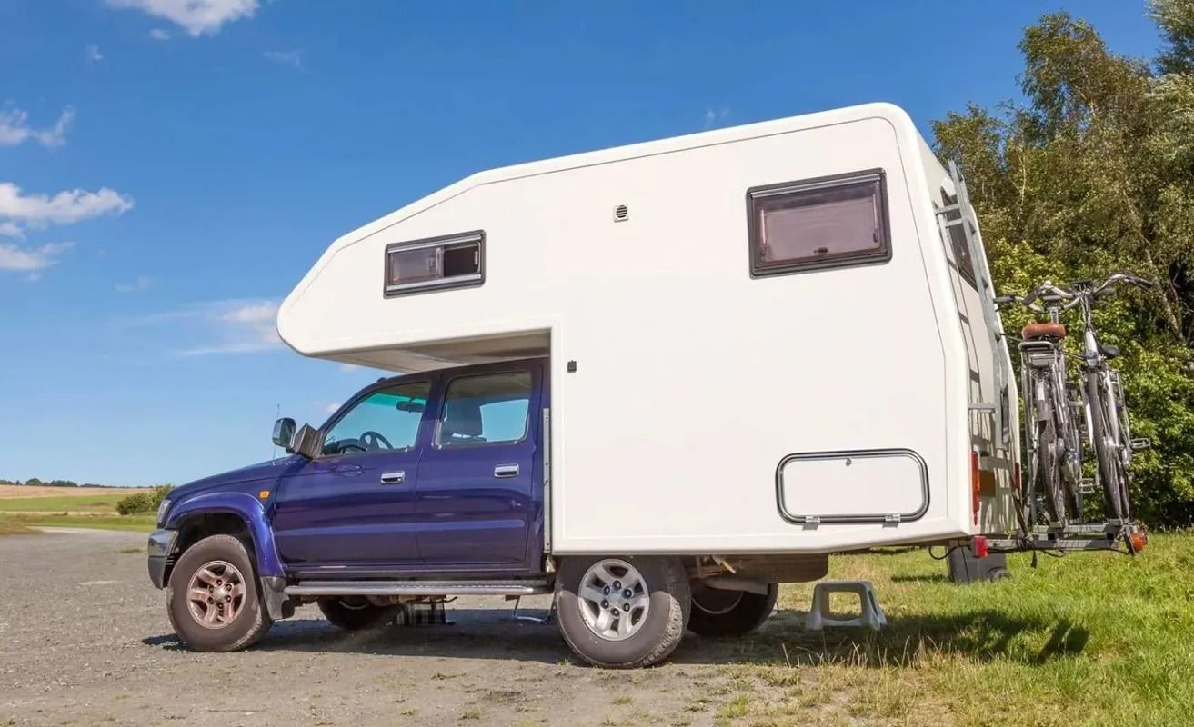 Blue pickup truck with white camper, parked on grass; bicycles on rear.