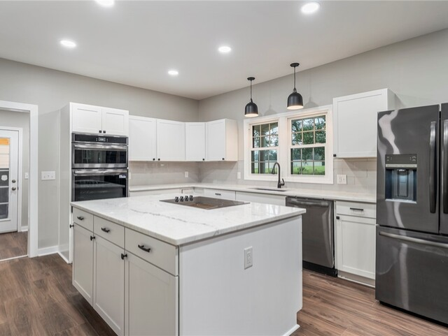 Modern white kitchen with island, stainless steel appliances, and two black pendant lights.