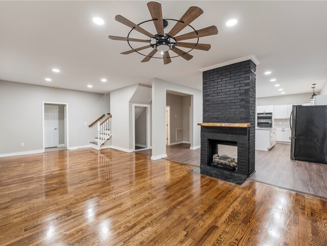 Spacious living room with hardwood floors, a black fireplace, and a large ceiling fan.