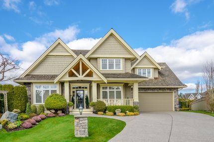 Beige house with a green lawn and driveway under a blue sky.