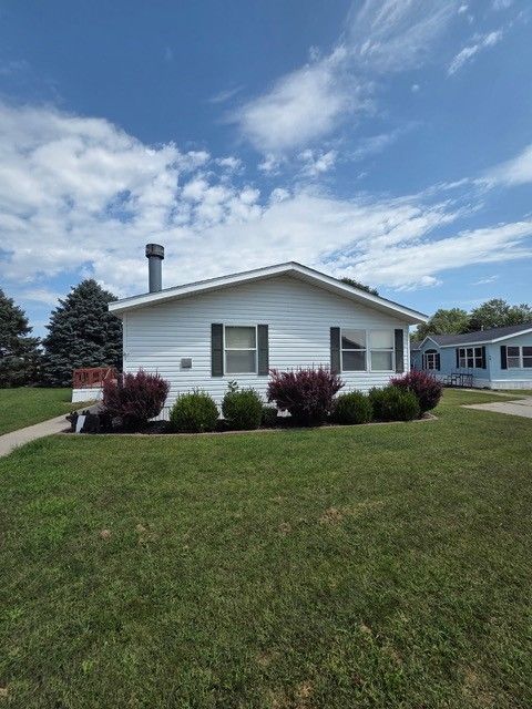 White house with green lawn, dark shrubs, and a blue sky with clouds.