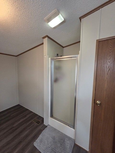 Bathroom with a shower, door, and wood-look flooring. White walls, brown trim, and a rug.