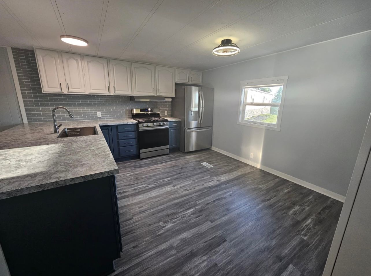 Modern kitchen with gray cabinets, stainless steel appliances, and dark wood-look flooring.