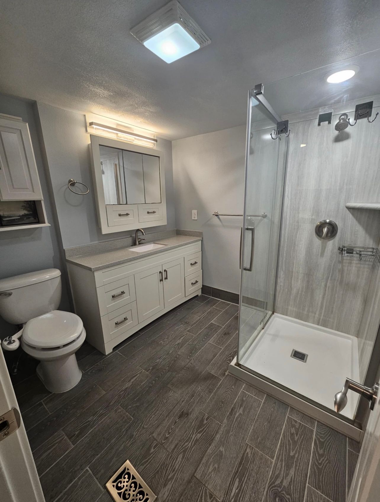 Gray and white bathroom with a glass shower, vanity, toilet, and gray tile flooring.