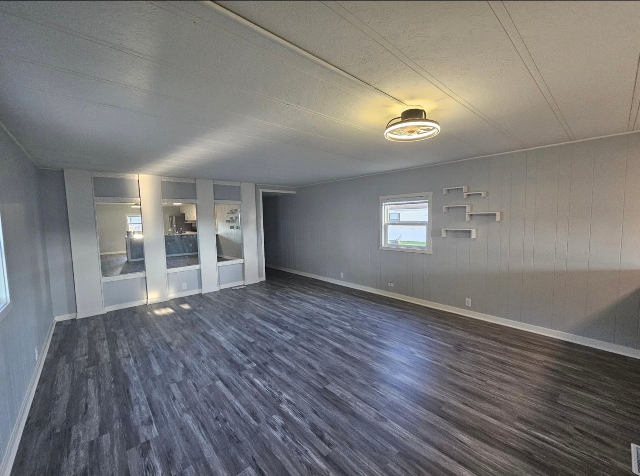 Empty living room with gray walls, wood-look floor, and a light fixture.