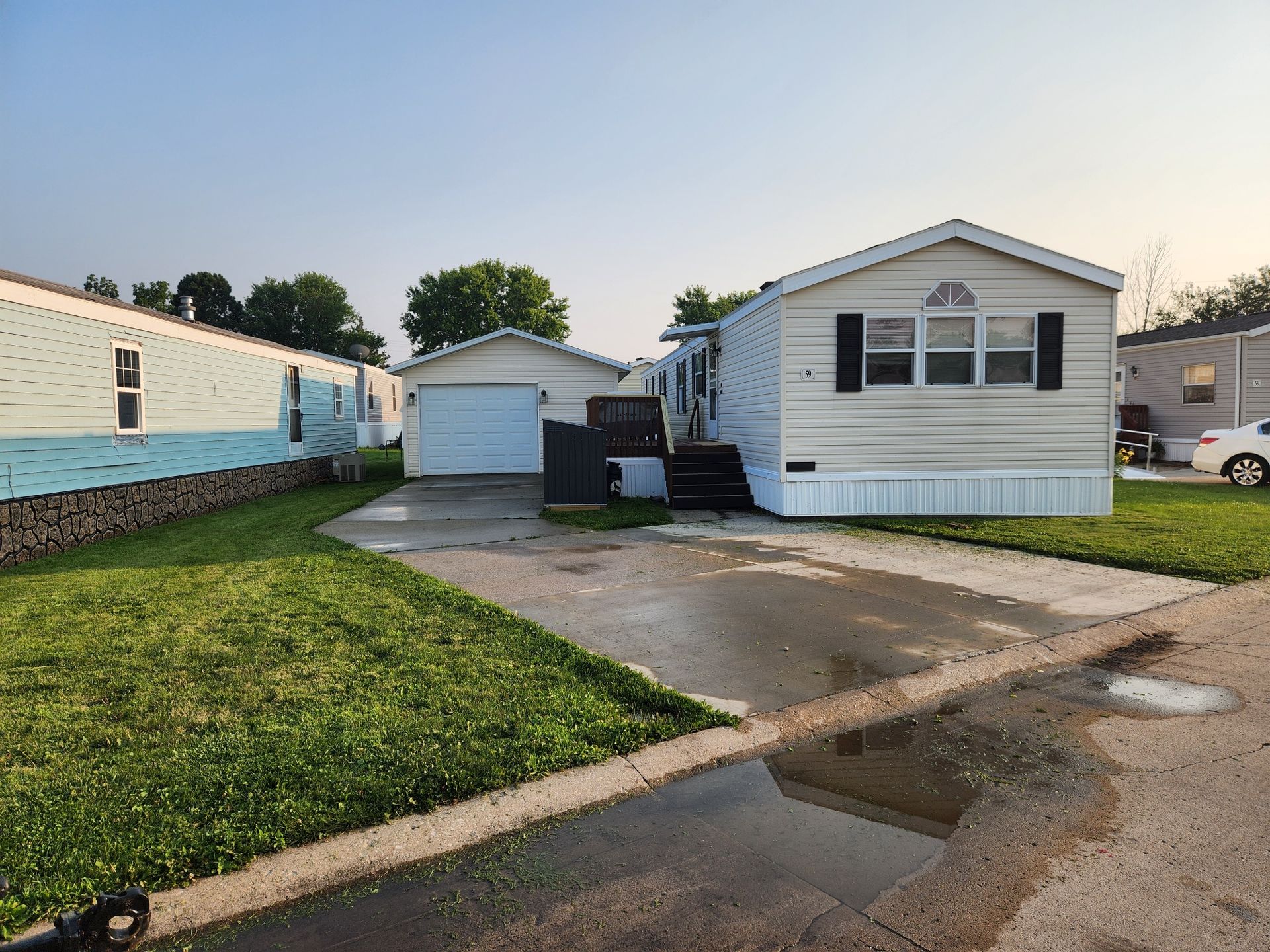 Mobile home with attached garage and a driveway, next to other mobile homes.
