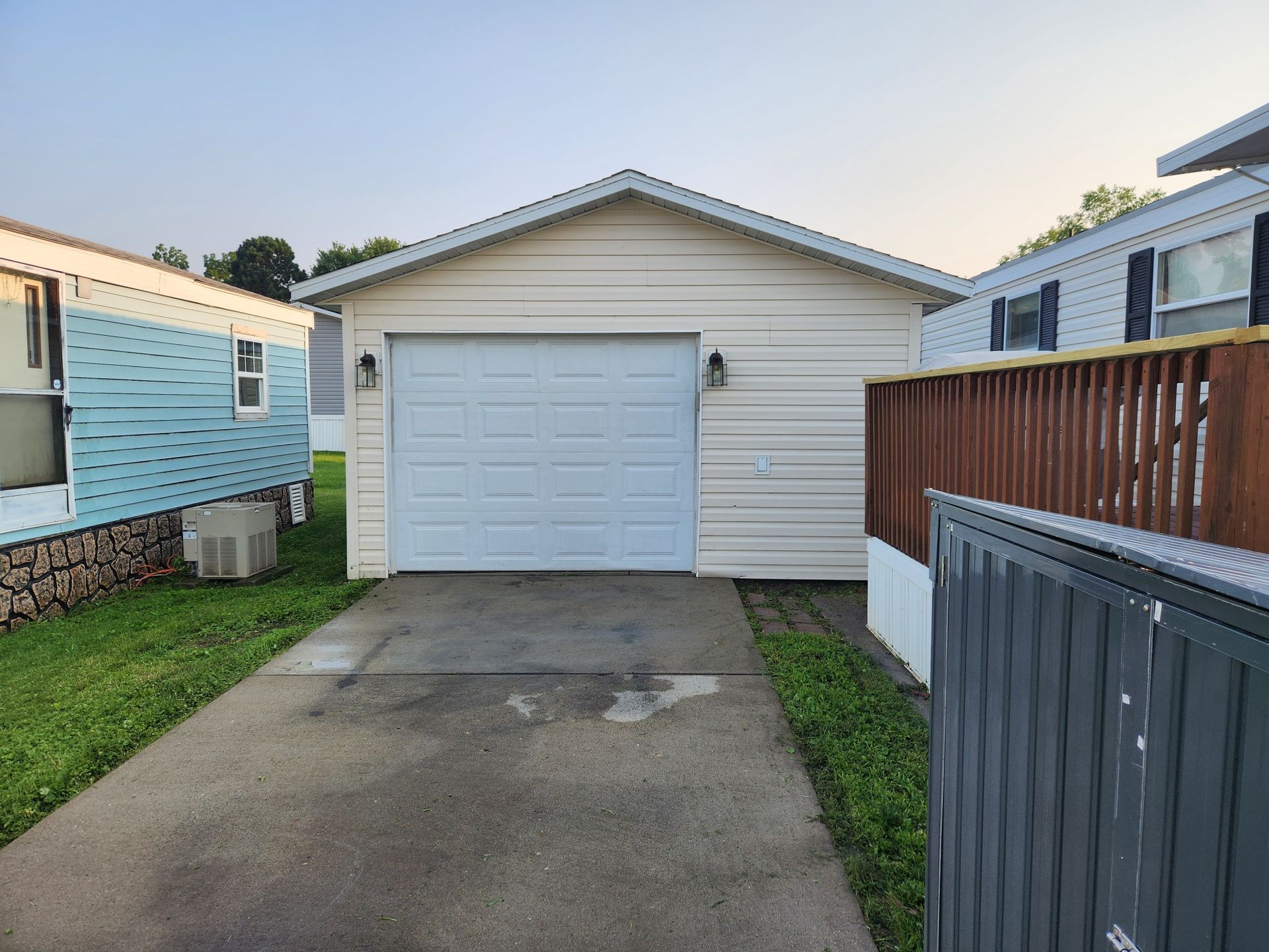 A light-colored garage with a closed white door, surrounded by mobile homes and a concrete driveway.