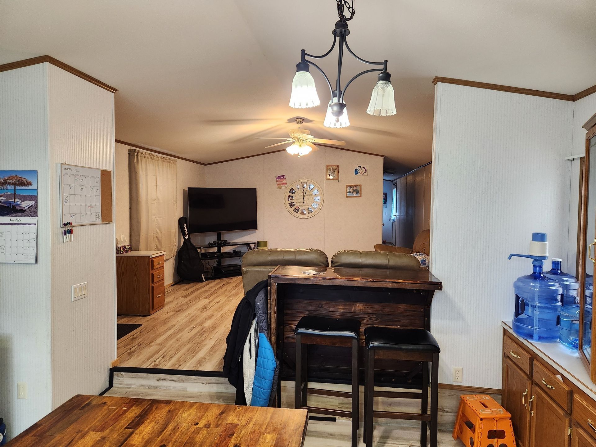 Interior view of a home with a bar, TV, and kitchen. Light wood floors and white walls are featured.