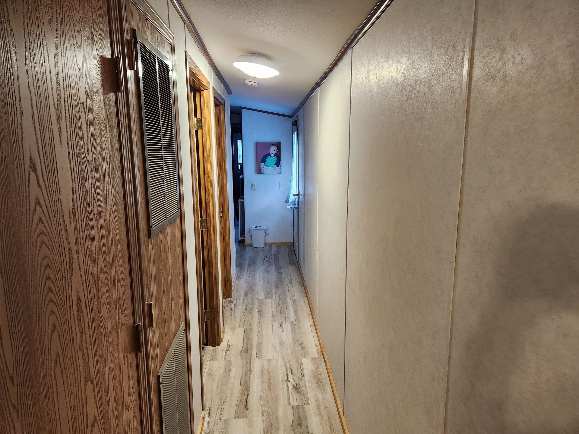Narrow hallway with wood-paneled door on left, light vinyl flooring, and doors leading to rooms.
