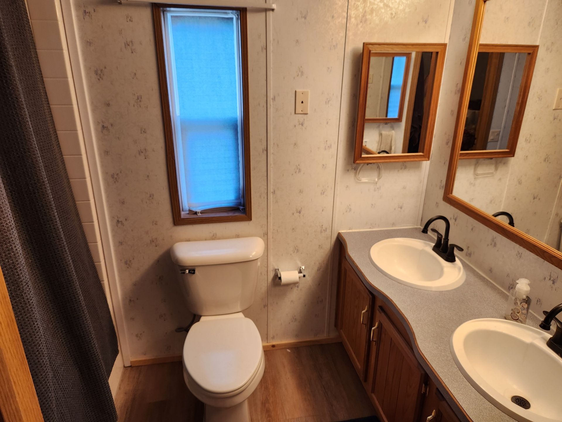 Bathroom with toilet, double sinks, and wooden cabinets; floral wallpaper.