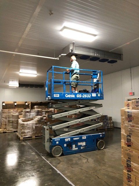 A man is standing on a scissor lift in a warehouse.
