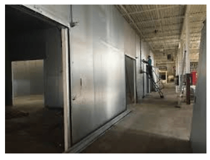 A man is standing on a ladder in an empty warehouse.