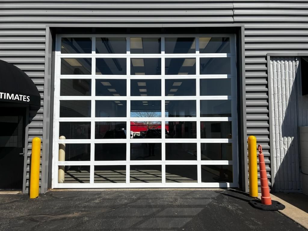 Garage door with white grid panels on a gray industrial building, flanked by yellow bollards and an orange cone