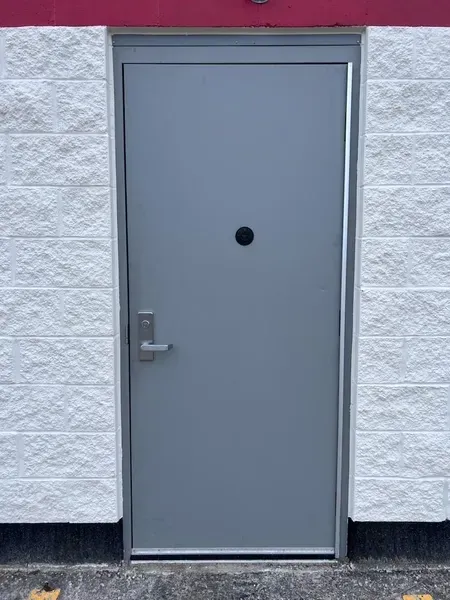 Gray metal door with a round peephole and handle in a white brick wall