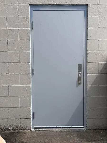 Gray metal door set in a cinderblock wall with a handle and hinges, viewed straight on.
