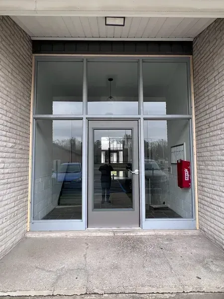 Glass entrance doors to a building lobby with white brick walls and a red fire extinguisher inside.