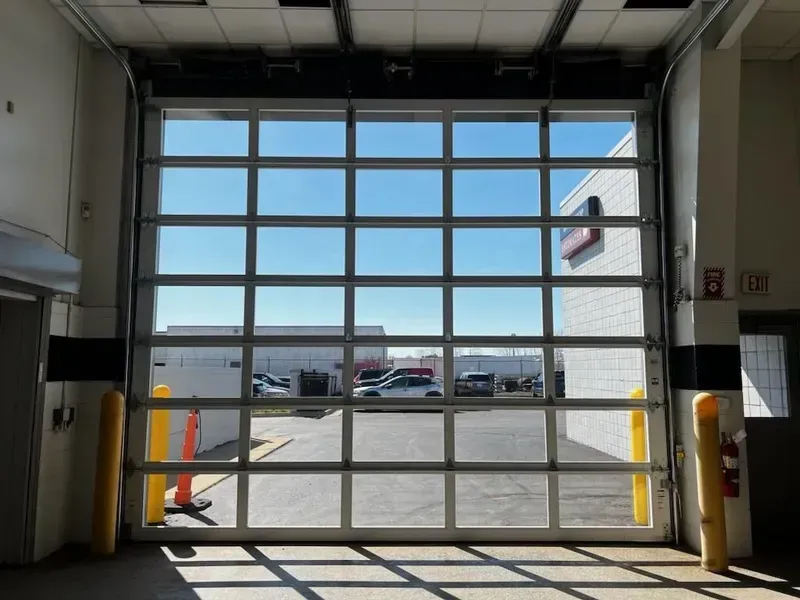 Interior view of a warehouse bay door opening to a sunny parking lot outside