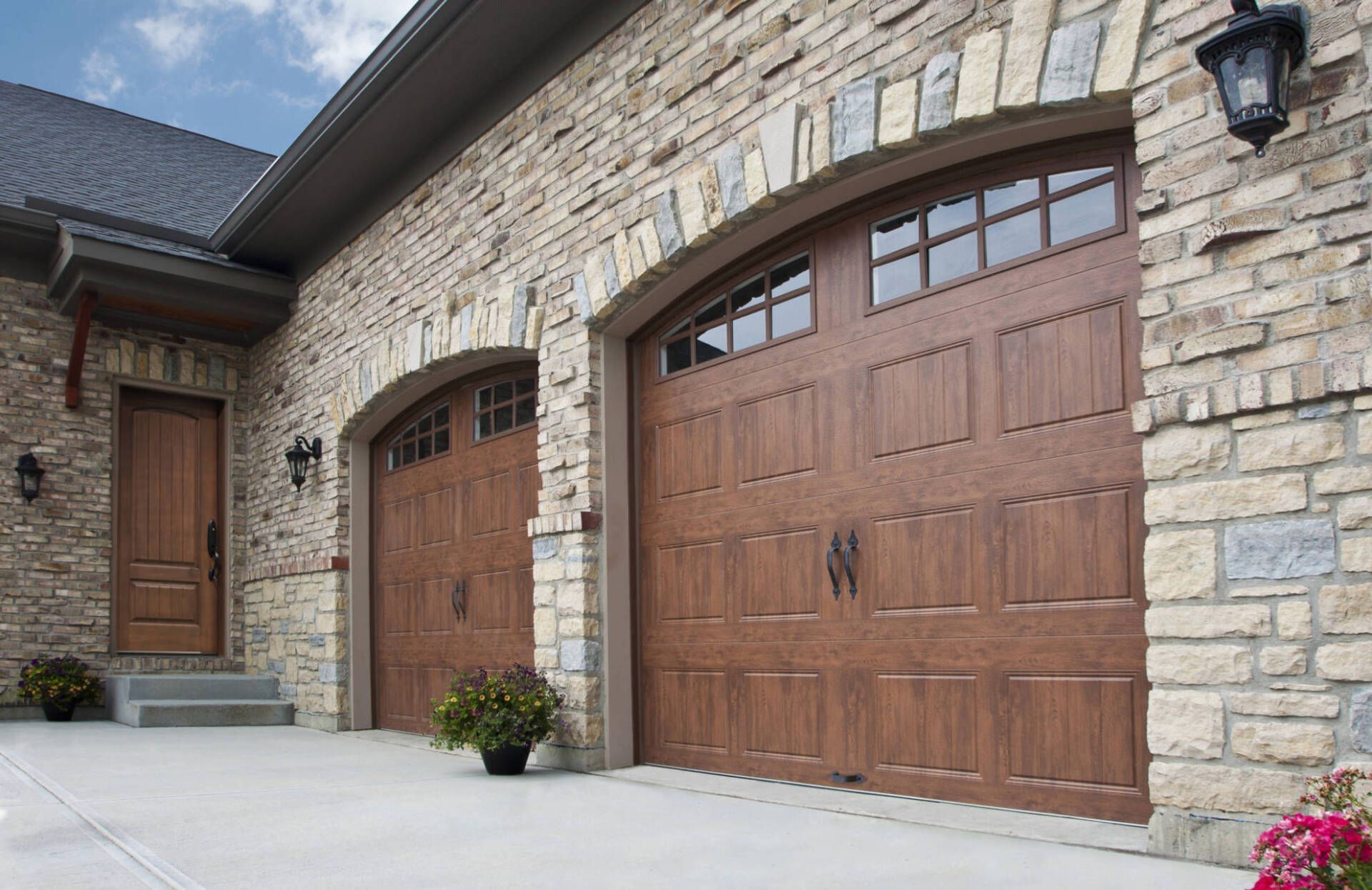 Stone house with two brown garage doors and a front entry, viewed from a driveway