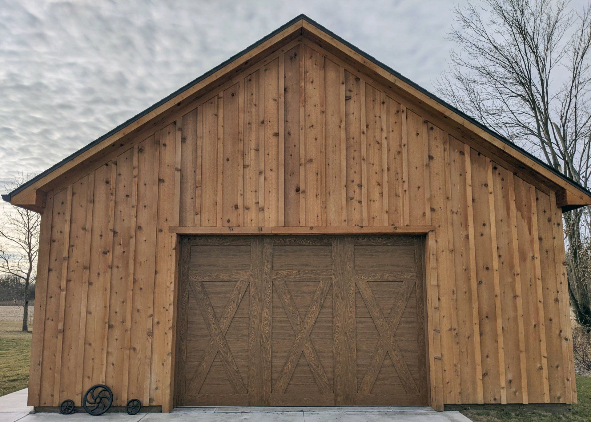 Wooden barn-style shed with a large brown garage door on a grassy lot.